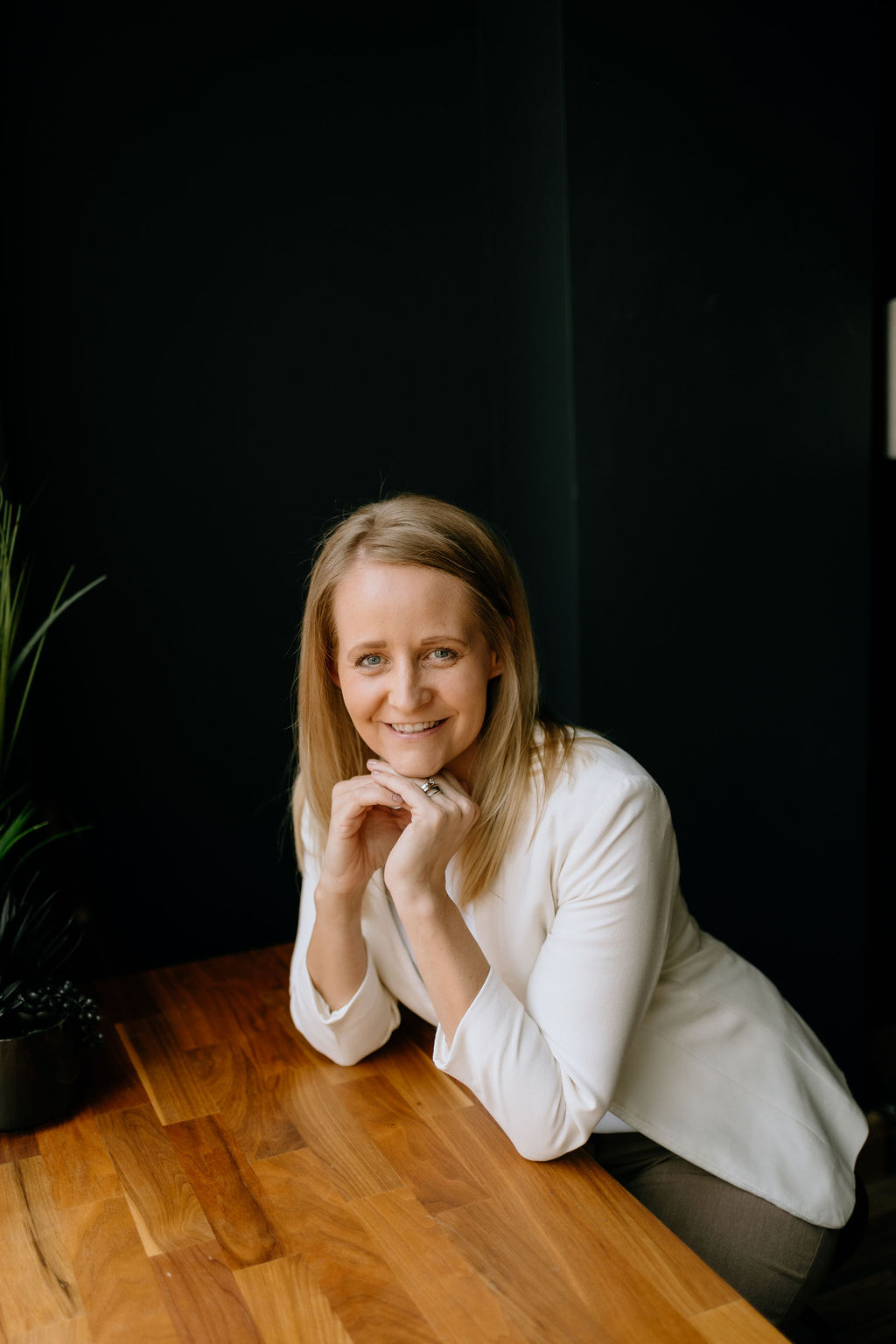Toni Schafer leaning on a wooden table, smiling warmly