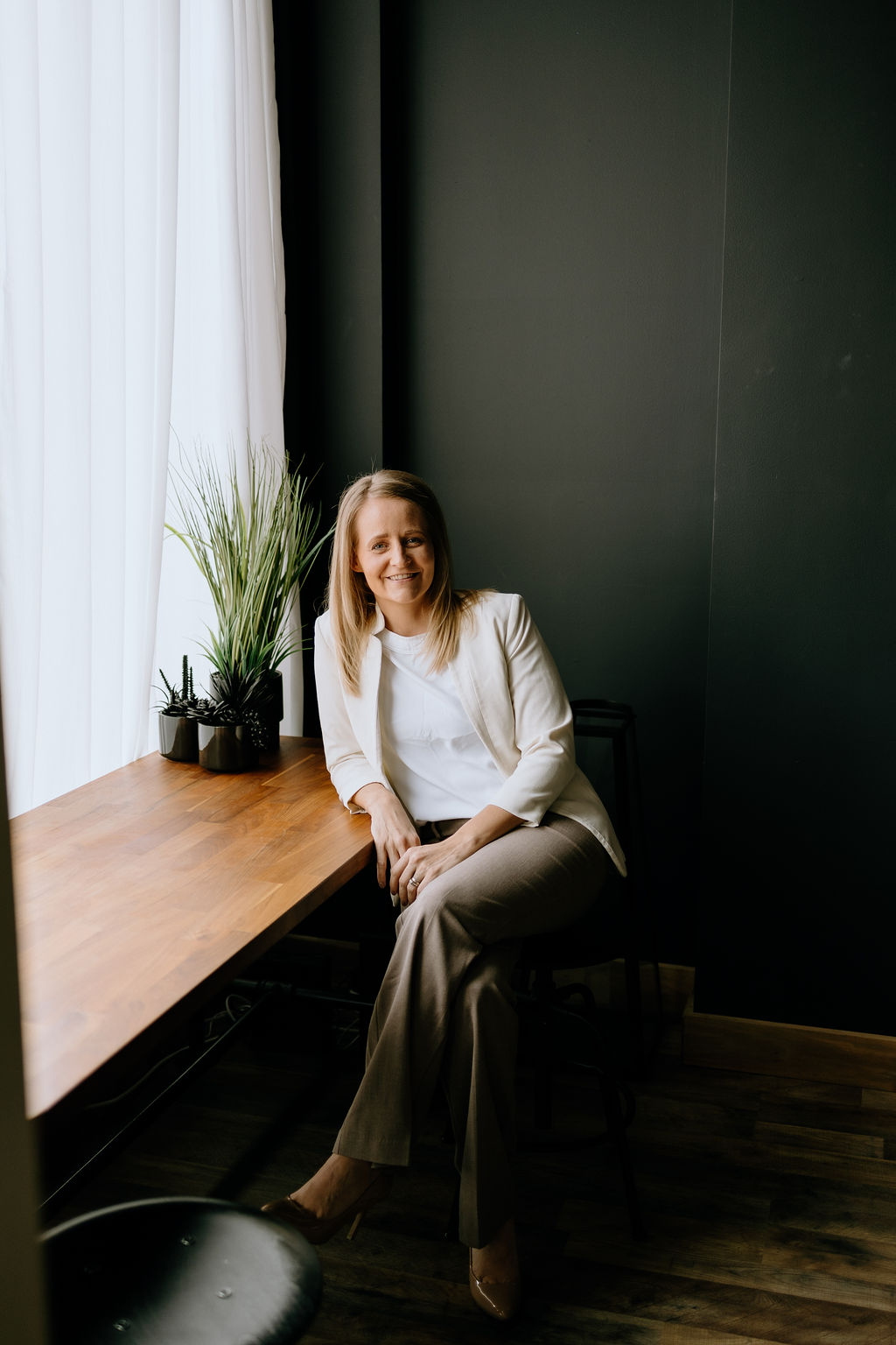Toni Schafer sitting at a wooden desk by a window, smiling — workshop facilitator and educator