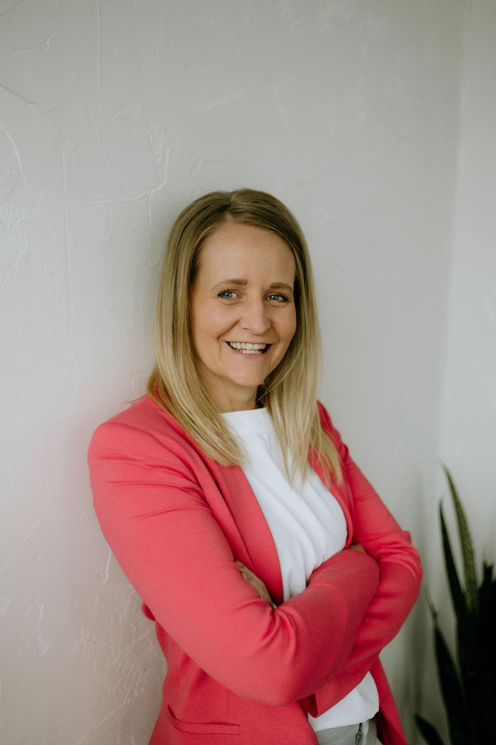 Toni Schafer smiling with arms crossed, wearing a coral blazer — real estate educator, speaker, and entrepreneur
